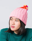 model wearing pink beanie with orange end and yellow, red, and pink pom