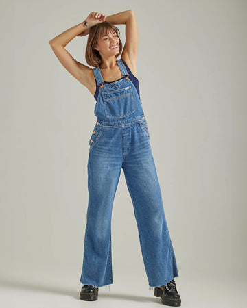 model wearing denim flare overalls with oversized front pocket and wrangler patch