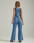 back view of model wearing denim flare overalls with oversized front pocket and wrangler patch