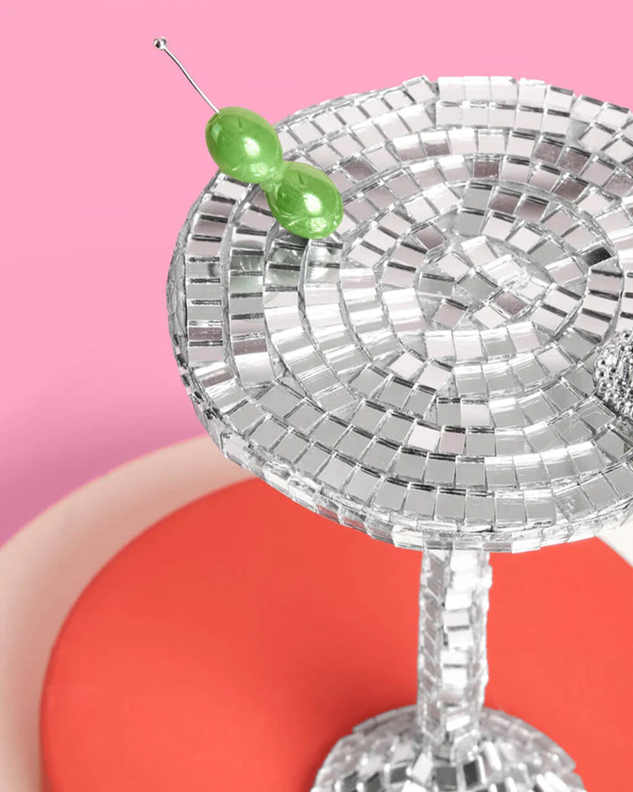 up close of disco martini glass shaped ornament with olive bead stirrer