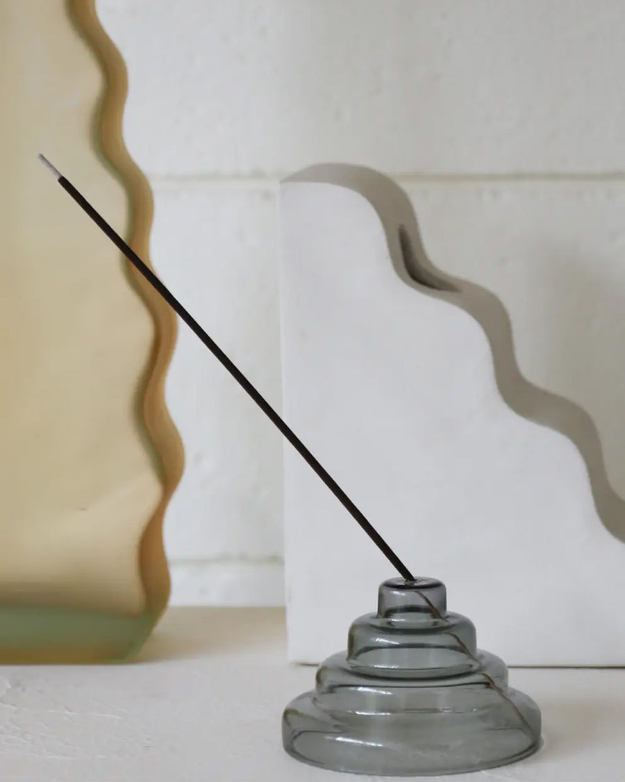 side view of grey stacked glass incense holder with an incense inside on a table