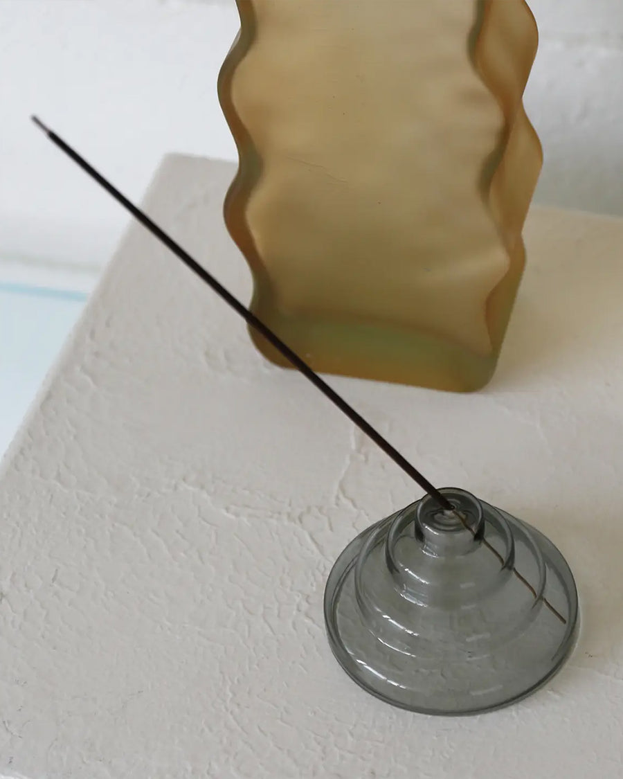 grey stacked glass incense holder with an incense inside on a table