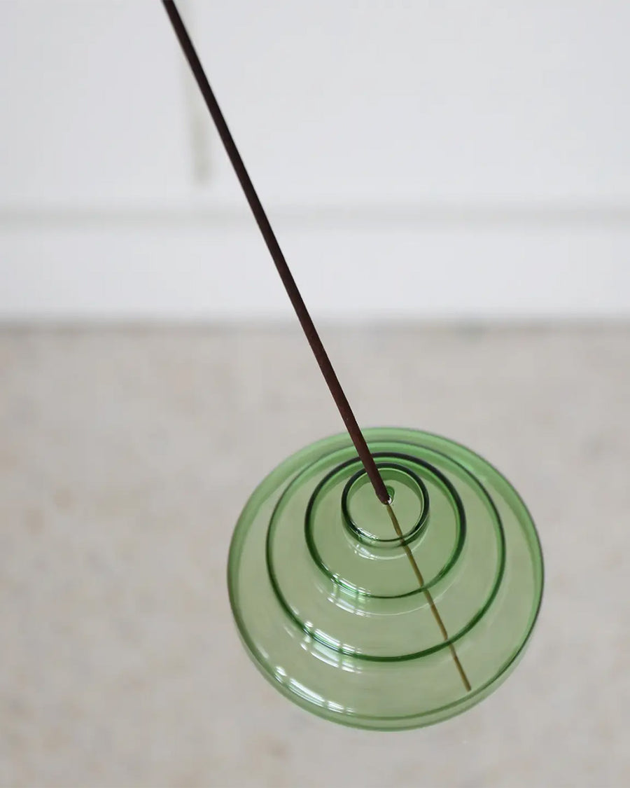 green stacked glass incense holder with an incense inside on a table