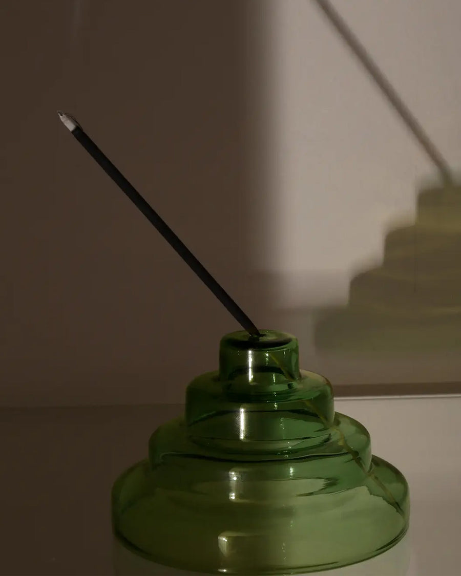 side view of green stacked glass incense holder with an incense inside on a table