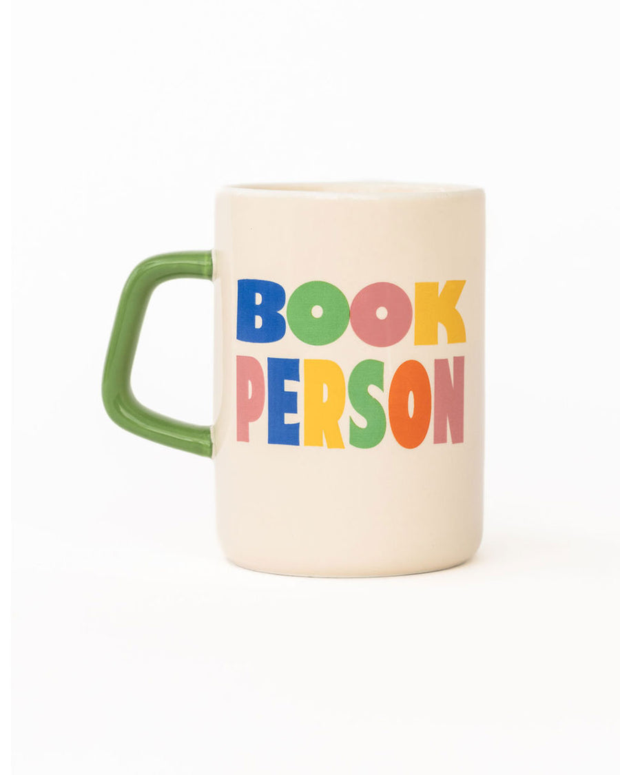 cream ceramic coffee mug with green handle and  colorful 'book person' across the front and smiley face inside
