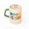 cream ceramic coffee mug with green handle and  colorful 'book person' across the front and smiley face inside
