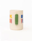 side view of cream ceramic coffee mug with green handle and  colorful 'book person' across the front and smiley face inside