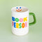 cream ceramic coffee mug with green handle and colorful 'book person' across the front and smiley face inside on green background