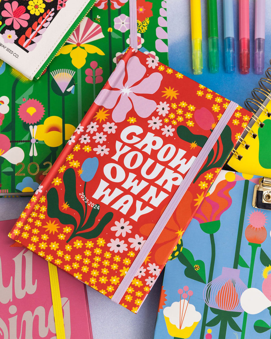 editorial image of 17-month classic planner with red ground, colorful abstract flowers and white 'grow your own way' text across the front
