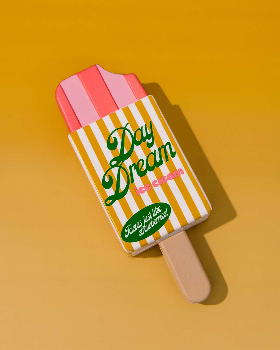 popsicle shaped de-stress ball with yellow and white stripe label that says 'day dream ice cream: tastes like strawberries!' on orange background