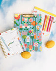 clipboard folio with blue ground and colorful abstract floral print with notepad and planner next to it