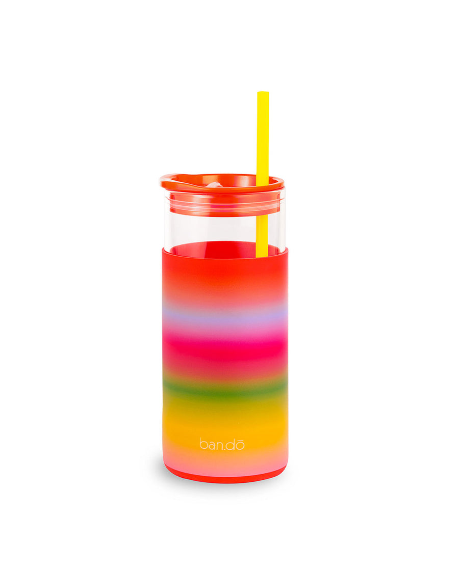 backview of glass 20 oz tumbler with red lid, yellow straw, and rainbow ombre sleeve with white text 'make time to make magic' across the front