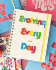 editorial image of 12 month medium planner with cream cover and colorful 'evolving everyday' text and yellow elastic closure