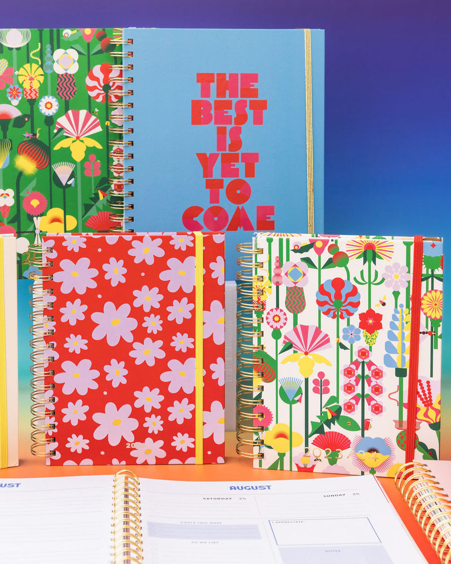 editorial image of 12-month planner with coral red cover with purple abstract flower print and yellow elastic closure strap
