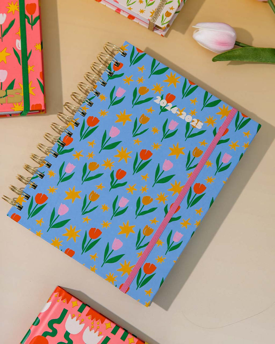 light blue 17-month planner with colorful tulip and star print on ombre ground surrounded by other planners