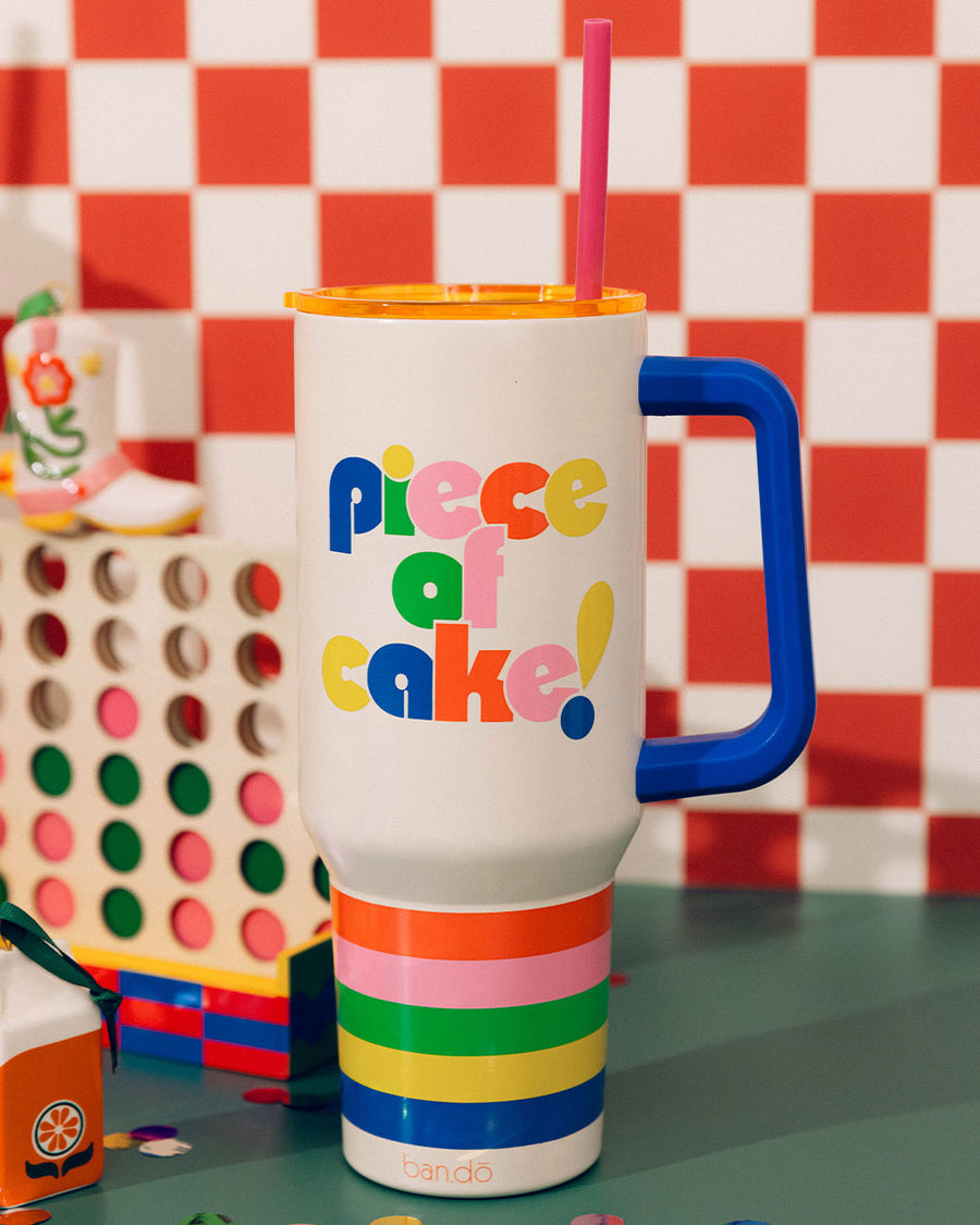 white mega 40 oz stainless steel tumbler with colorful 'piece of cake!' on the front against pink tile