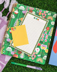 large rough draft notebook with green ground and vibrant abstract floral print with notepad on it