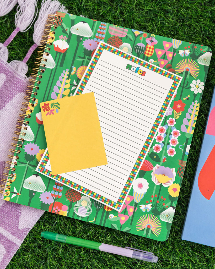 large rough draft notebook with green ground and vibrant abstract floral print with notepad on it