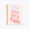 spiral bound notebook cover in blush pink with "ONE DAY AT A TIME" text graphic