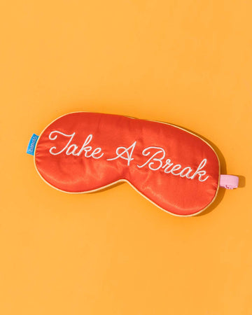 red satin eye mask with cursive 'take a break' across the front on orange background