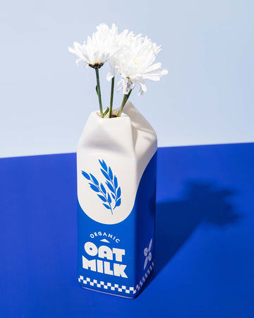white and blue carton shaped ceramic vase with 'organic oat milk' across the front with white flowers inside