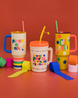 cream mega trucker cup with vibrant 'there's a party going on right here!' across the front, red lid, and yellow straw alongside two stainless steel tumblers