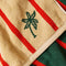 up close of tan and red vertical stripe towel with darn green reverse side and embroidered palm tree print
