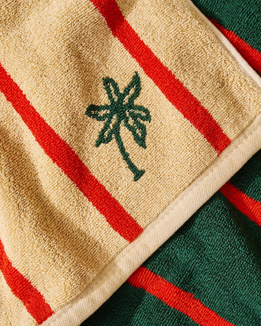 up close of tan and red vertical stripe towel with darn green reverse side and embroidered palm tree print