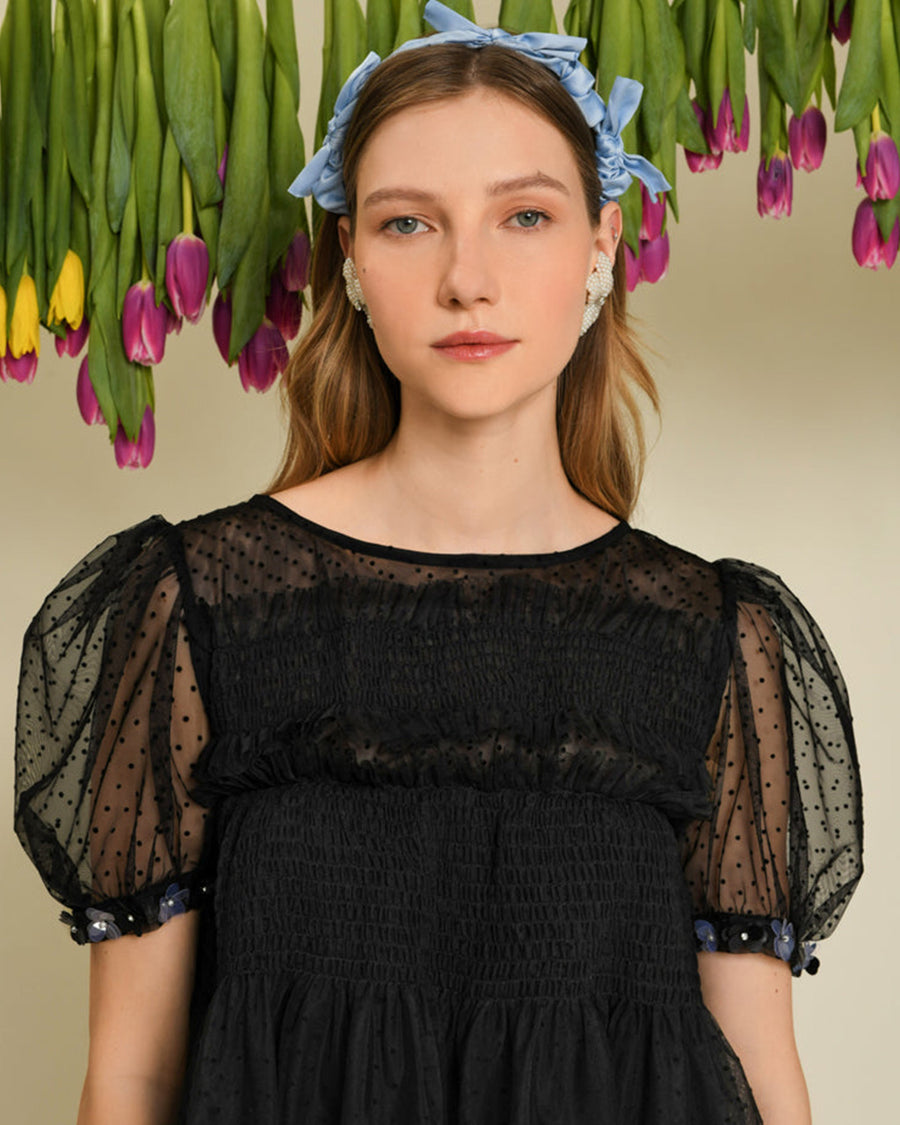 up close of model wearing black tulle cropped top with sheer puff sleeves, dot detail and embellished trim on sleeves