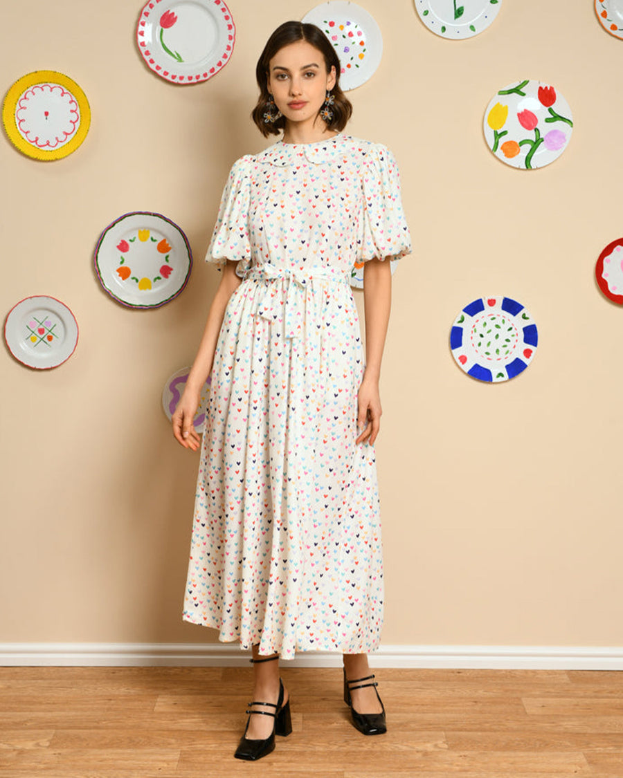 model wearing white midi dress with tie waist, slight puff sleeves and all over multi heart print