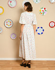 back view of model wearing white midi dress with tie waist, slight puff sleeves and all over multi heart print