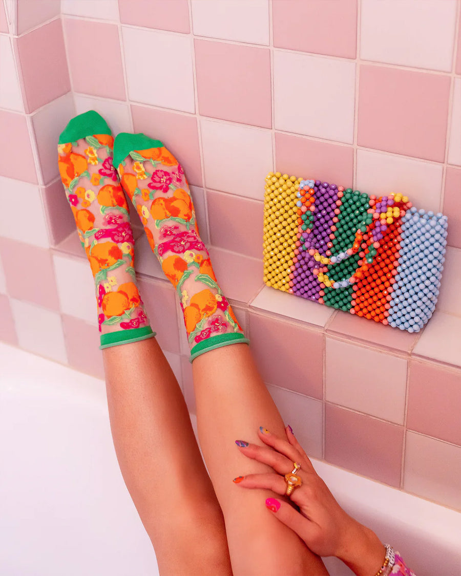 model wearing orange floral sheer socks next to a colorful purse