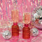 Tipsy Turvy Bar Glasses surrounded by tinsel and disco balls on a pink background