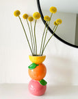 Stacked citrus vase on mantle with yellow round flowers