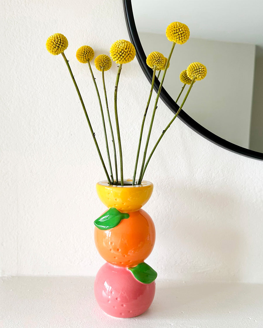 Stacked citrus vase on mantle with yellow round flowers