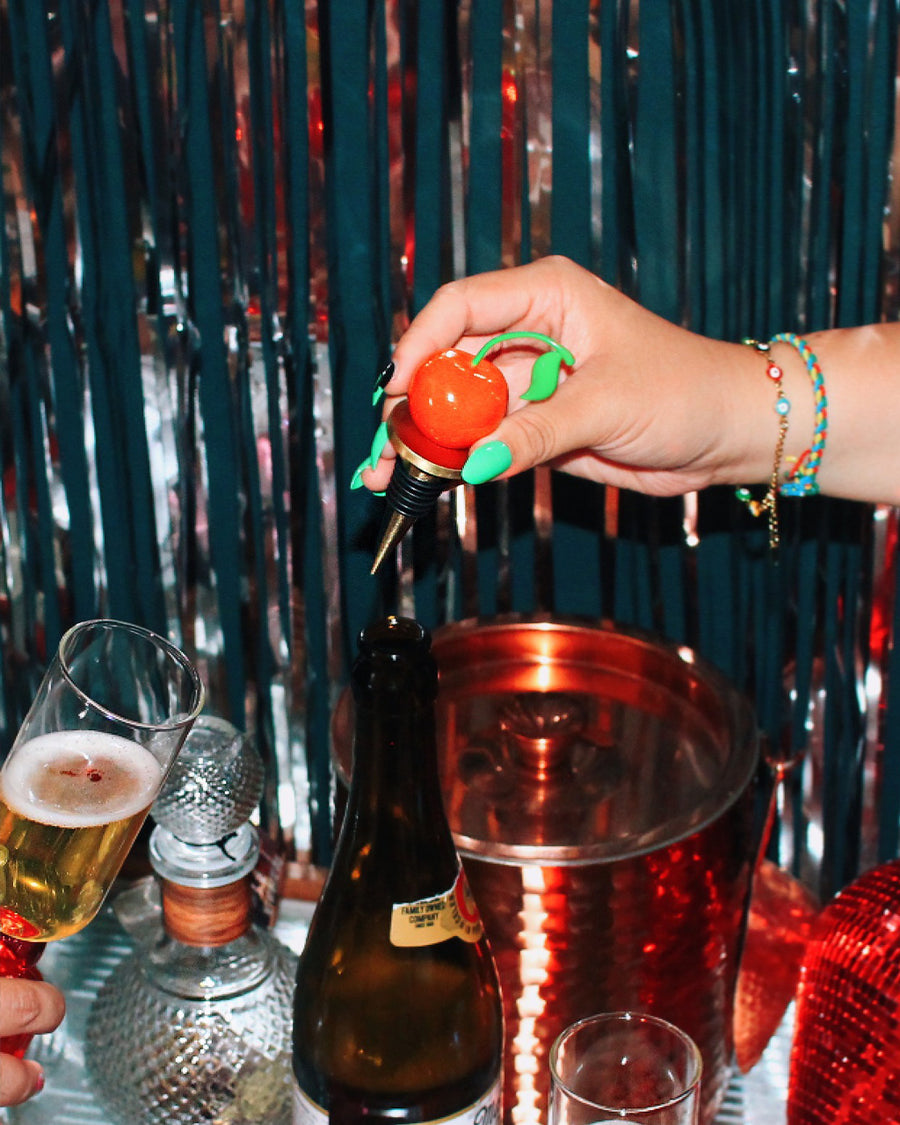 hand with green nail polish holding the cherry wine stopper, surrounded by drinks and tinsel