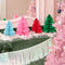 accordion paper christmas trees on a mantle beside a pink christmas tree