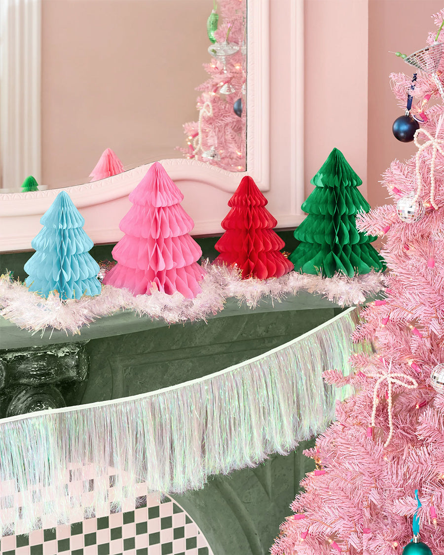 accordion paper christmas trees on a mantle beside a pink christmas tree