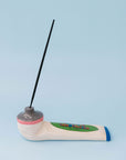 Incense holder in the shape of a paint tube, with a stick of incense, on a blue background