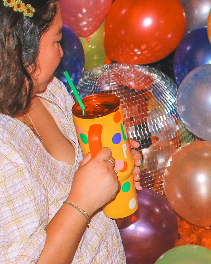 Woman holding yellow Life of the Party Tumbler surrounded by balloons and a disco ball