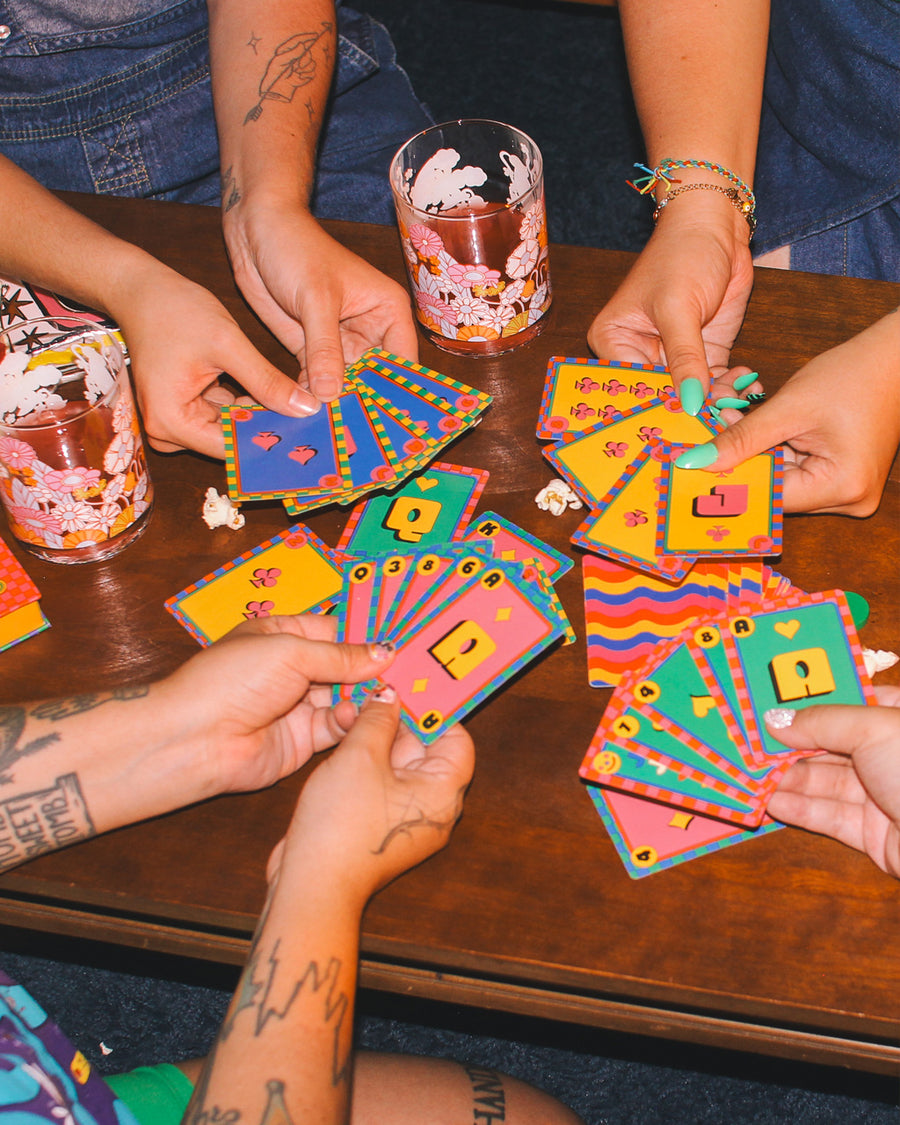 Four sets of hands holding playing cards at a table with drinks