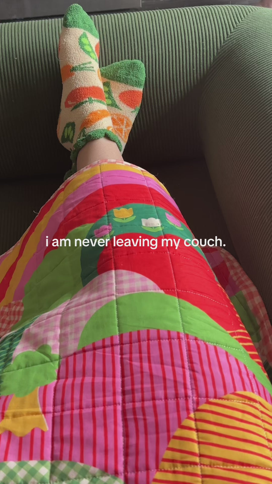 model wearing cozy veggie socks and throw blanket and says 'i'm never leaving my couch'