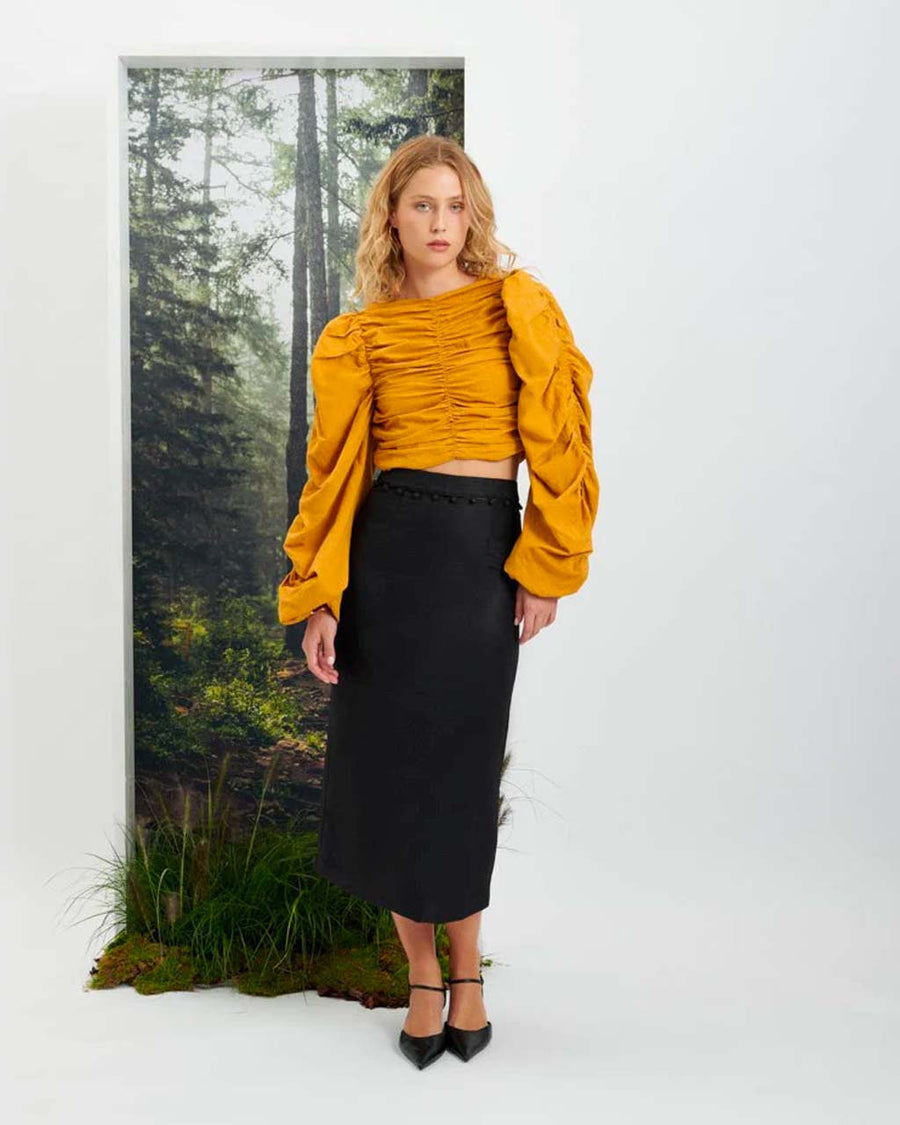 Full view of model wearing a mustard colored shirt and black midi skirt