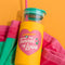 glass tumbler with yellow sleeve that says 'i got smooched at the tunnel of love', green lid and pink straw on a yellow background on top of a green and pink towel