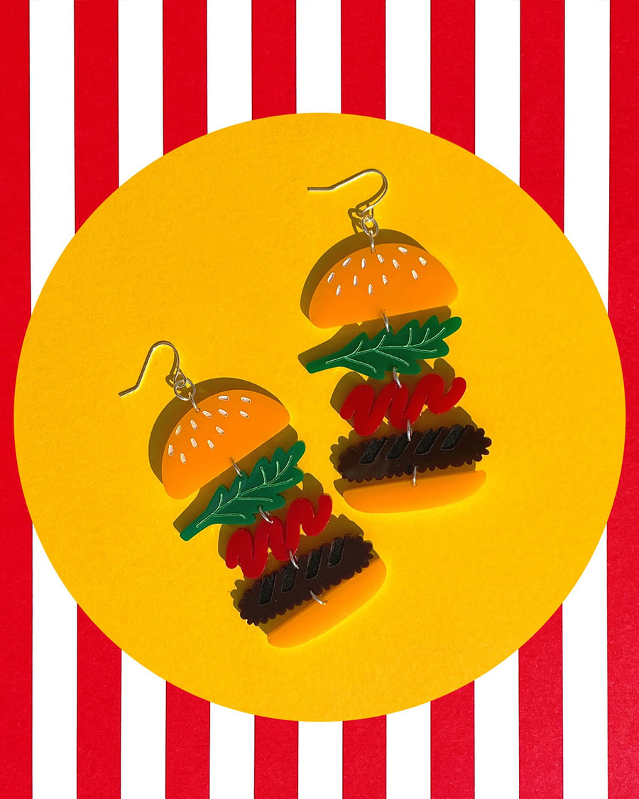 pair of burger drop earrings with sesame seed bun, lettuce, ketchup squiggle and patty. made from acrylic
