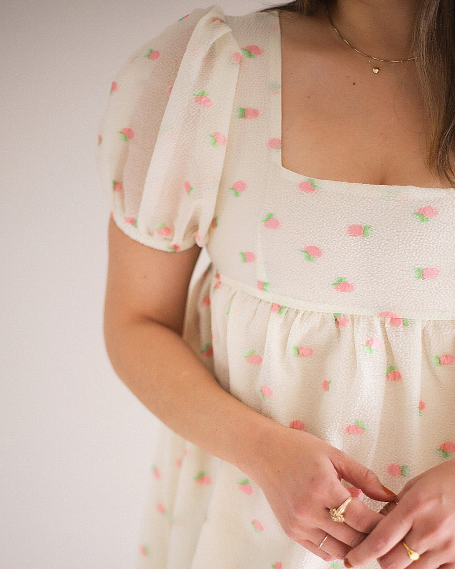 up close of model wearing white mini dress with puff sleeves and all over pink fruit print