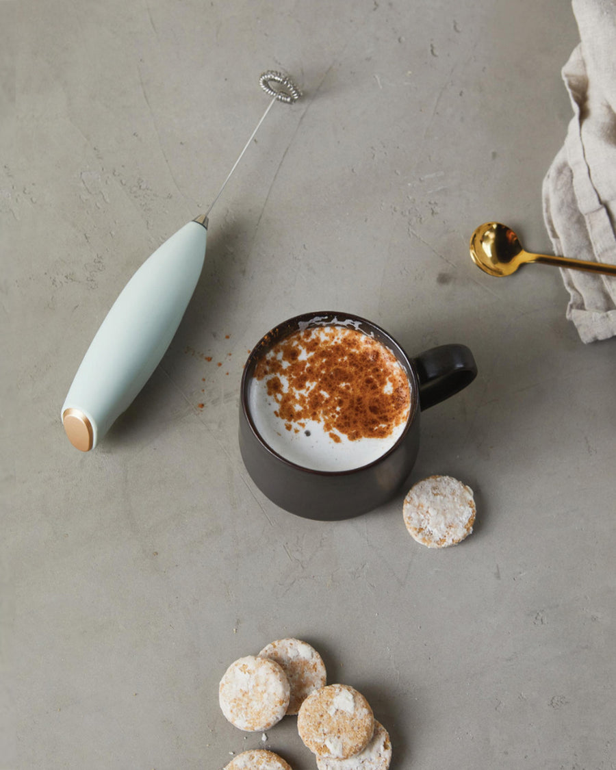 editorial image of  mint electric milk frother with gold accents and coffee drink