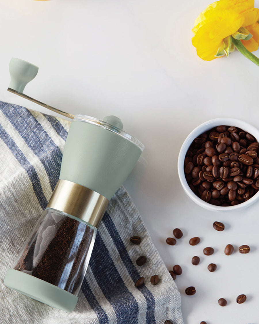 editorial image of the sage hand grinder, coffee beans, tea towel and yellow flower