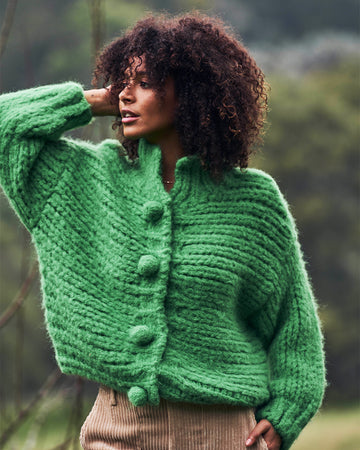 model wearing green chunky knit cardigan with large buttons and brown corduroy pants