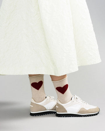 model wearing beige crew socks with maroon hearts on ankles with white and tan sneakers and white skirt